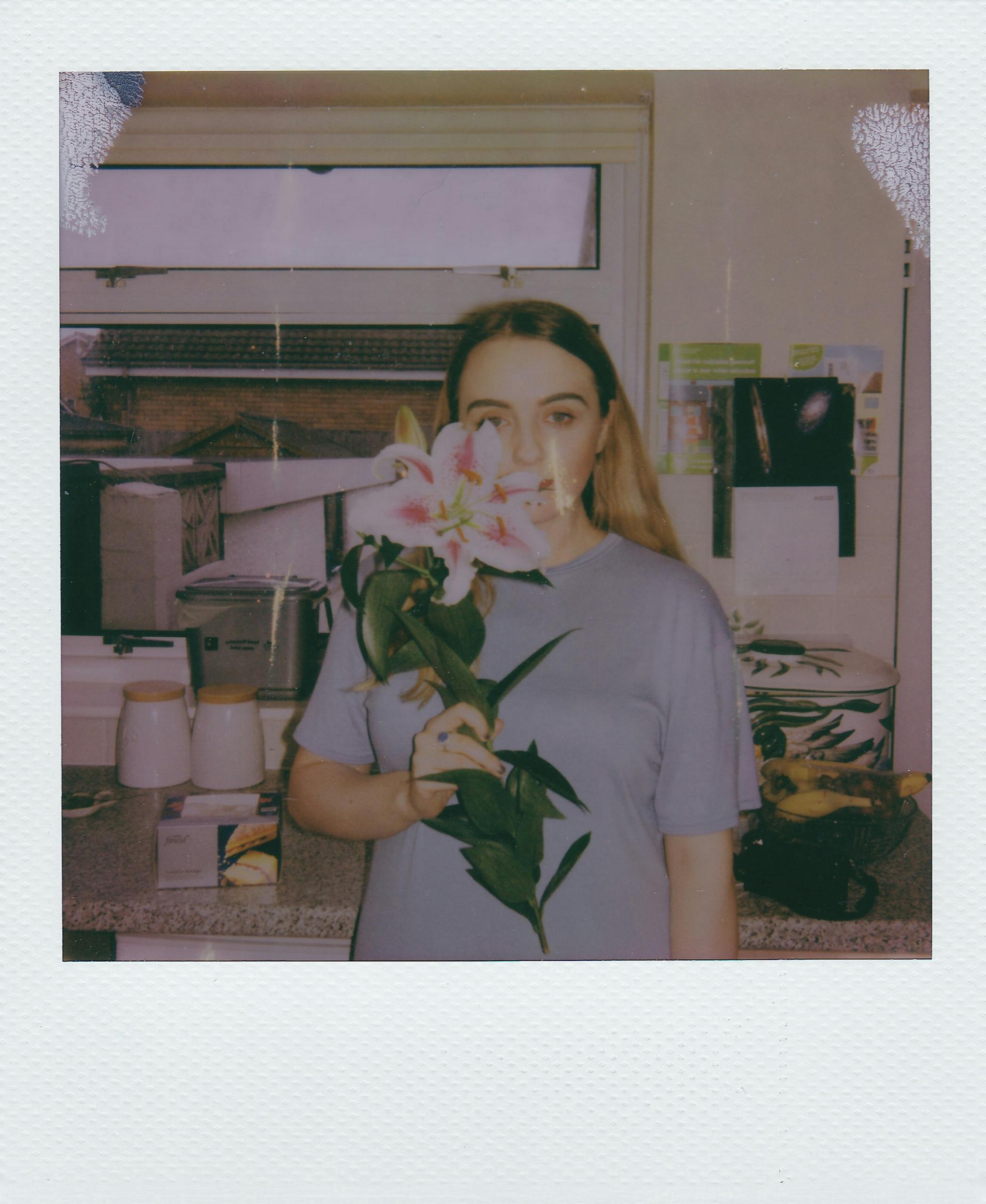 A woman in a kitchen holding a pink lily flower, creating a serene indoor atmosphere.
