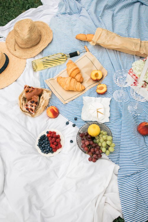 Free A delightful picnic setup featuring fresh fruits, croissants, and a sun hat on a striped blanket. Stock Photo