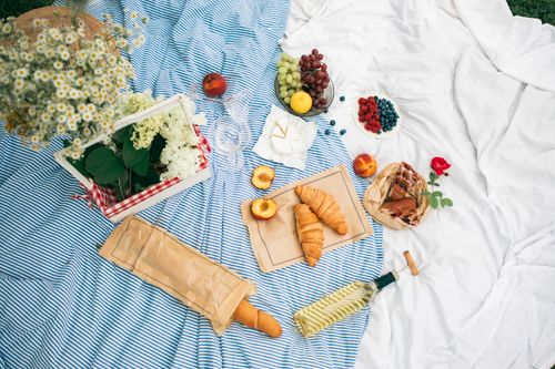 Free A delightful summer picnic spread with wine, croissants, fresh fruits, and flowers on a striped blanket. Stock Photo