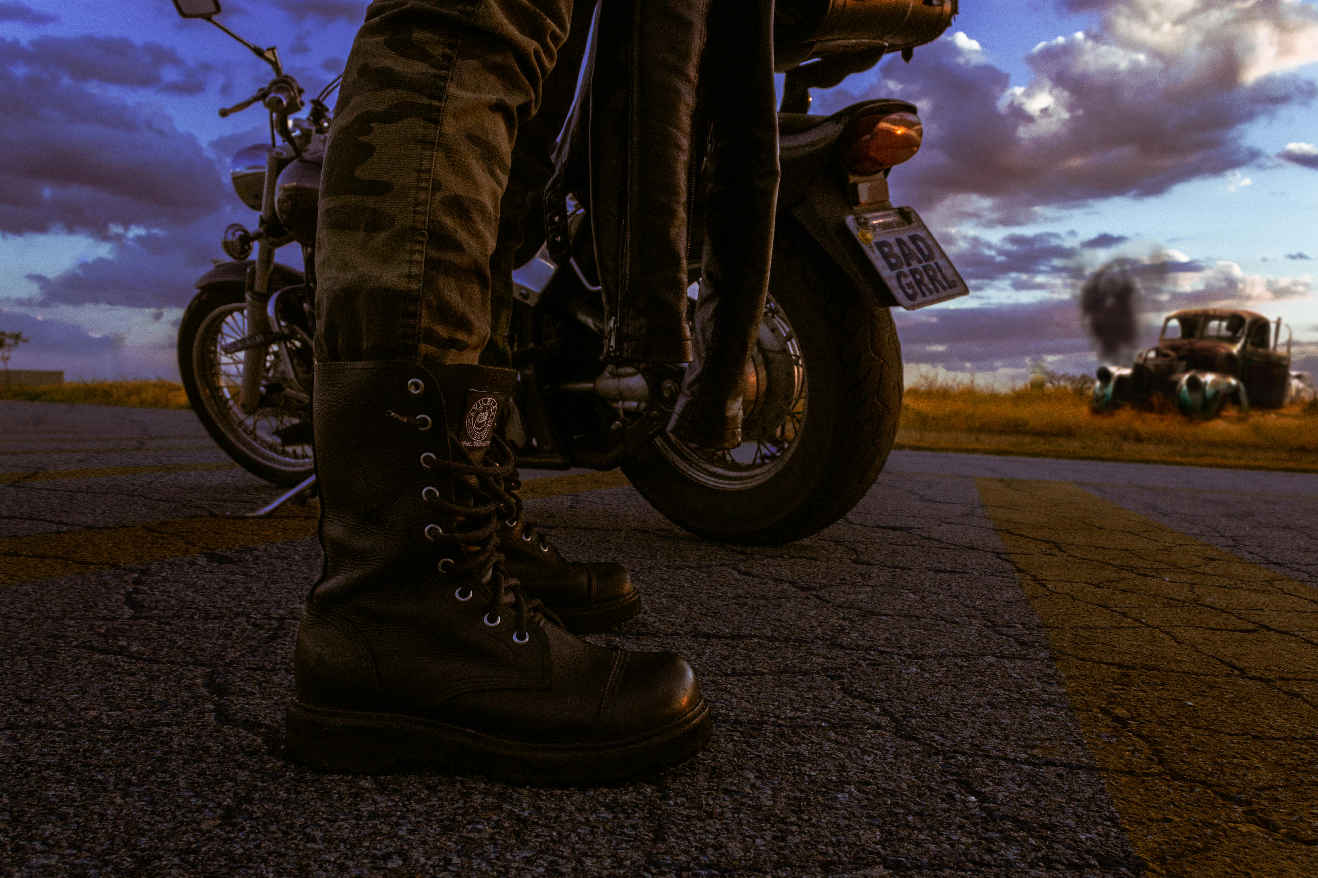 Close-up of black leather boots and motorcycles on a deserted road at dusk.