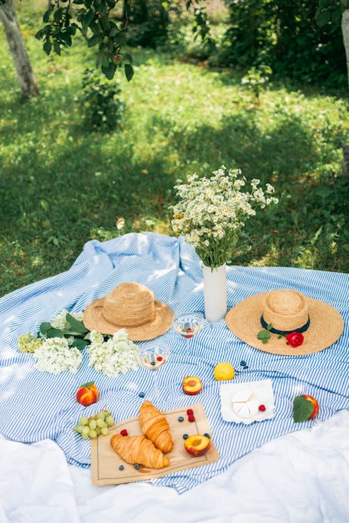 Food Beside the Flowers and Straw Hats on a Picnic Blanket