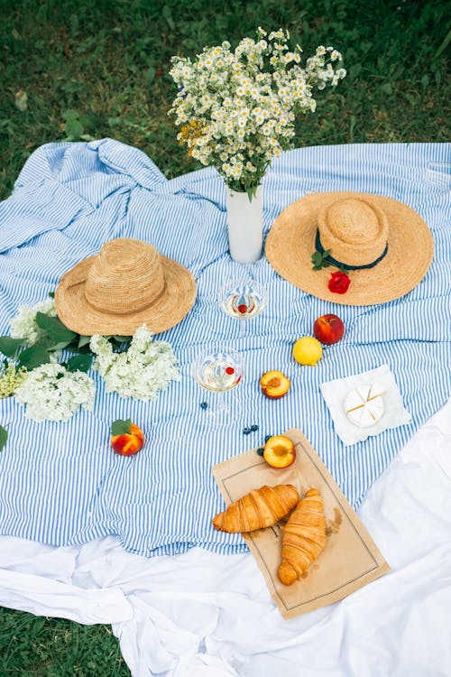 Food and Wine Beside the Flowers and Straw Hats on a Picnic Blanket