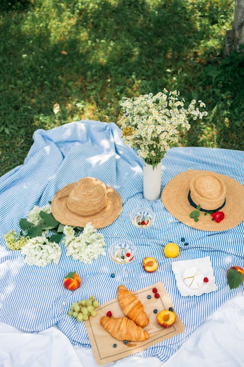 Food and Wine Beside the Flowers and Straw Hats on a Picnic Blanket
