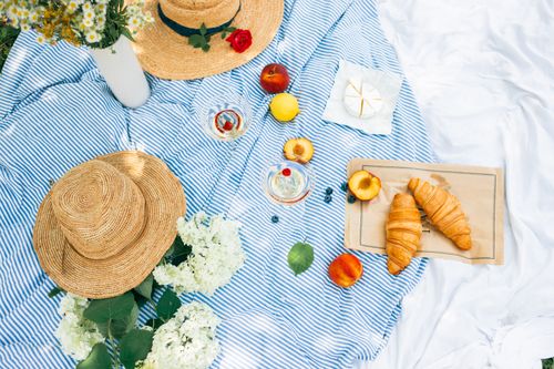 Free Charming summer picnic setup with croissants, fruits, and straw hats on a blue blanket. Stock Photo