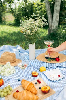 夏季野餐很惬意，条纹毯子上摆着羊角面包、水果、布里奶酪和白葡萄酒