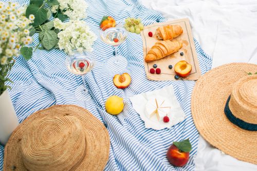 Free Charming summer picnic featuring wine, croissants, and fresh fruits on a striped blanket. Stock Photo