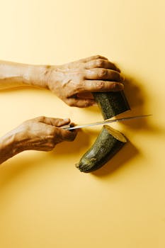 Hands slicing fresh zucchini on a vibrant yellow background, emphasizing healthy cooking.