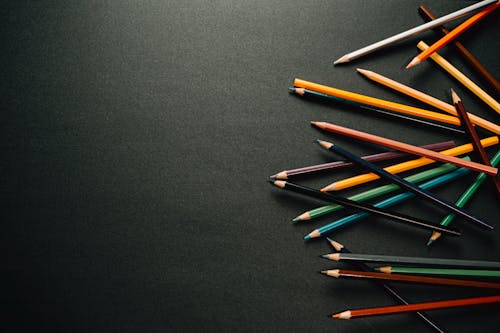 Free From above of colourful pencils scattered on dark surface in contemporary dark studio while placed on each other on black background Stock Photo