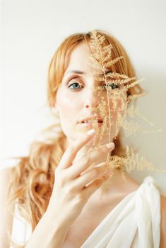 一位女士的肖像中，她手持一片精致的干叶，背景是柔和的白色