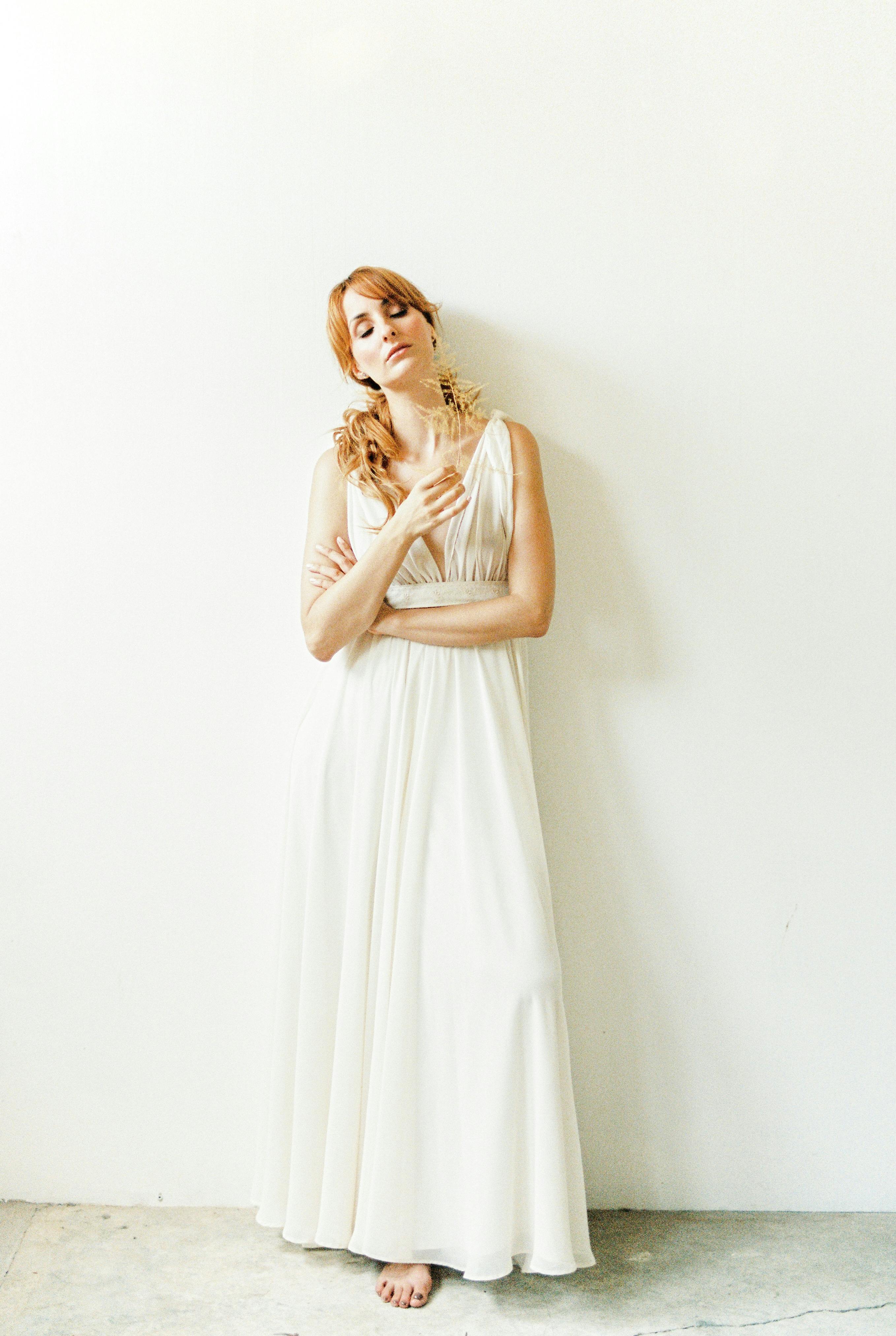在宁静的工作室里，一名身穿白色礼服的女子若有所思地对着白墙摆姿势