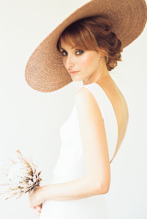 Free Elegant portrait of a woman in a white dress, wearing a wide-brimmed straw hat and holding a dried flower bouquet. Stock Photo