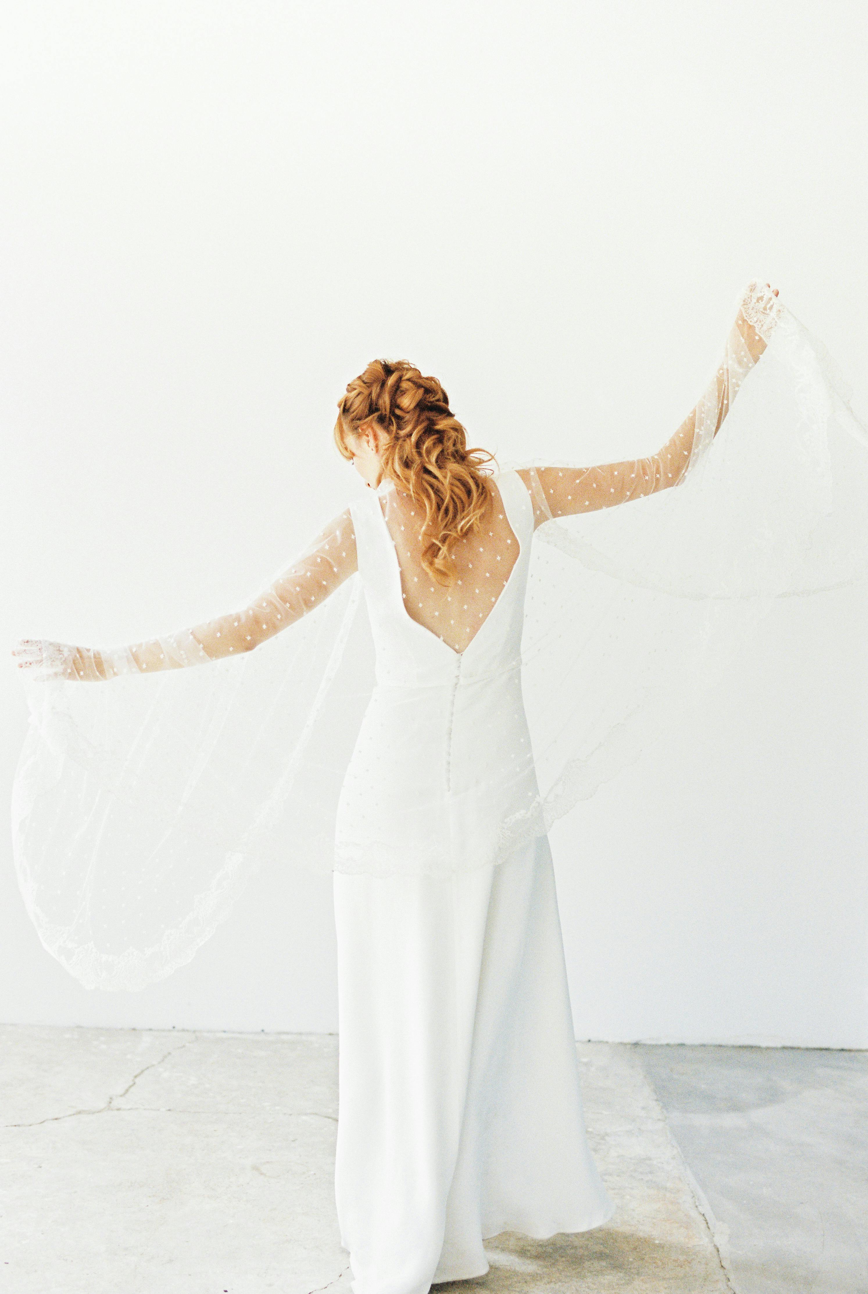 在明亮的工作室中，一名身穿优雅白色连衣裙的女子正摆出背影姿势