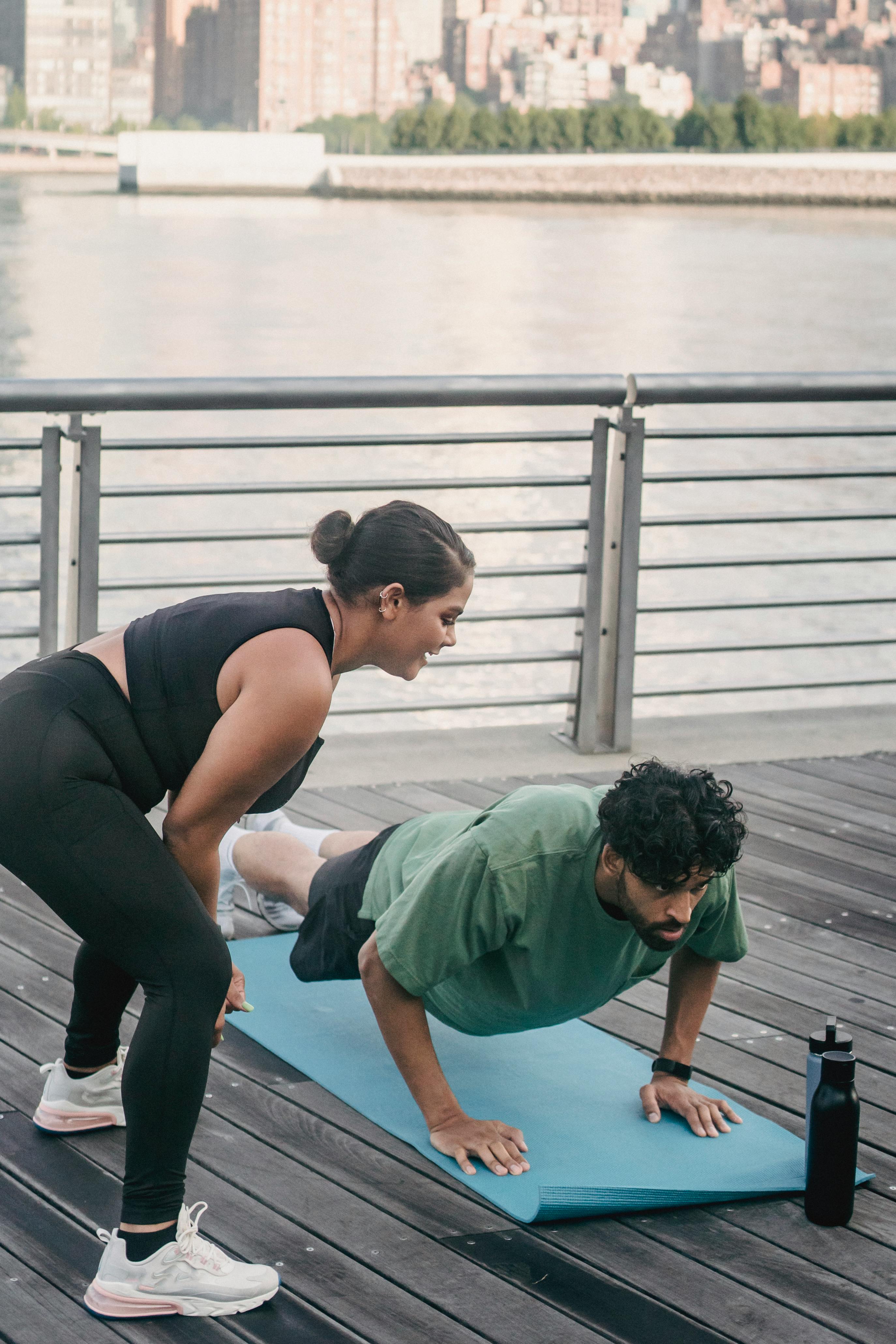 男女在水边的甲板上用瑜伽垫锻炼身体，促进健身