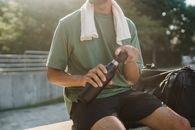 一名男子坐在户外，特写镜头对准了他手中的可重复使用水瓶和毛巾