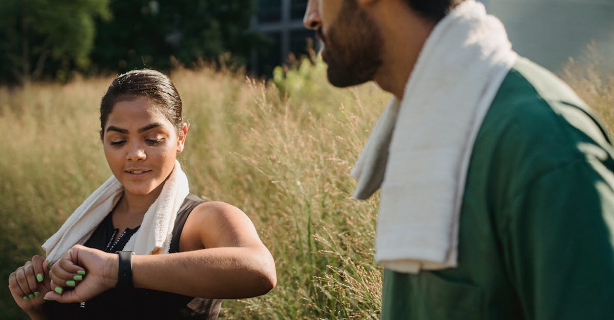 A couple outdoors using fitness trackers after a workout, wearing towels.