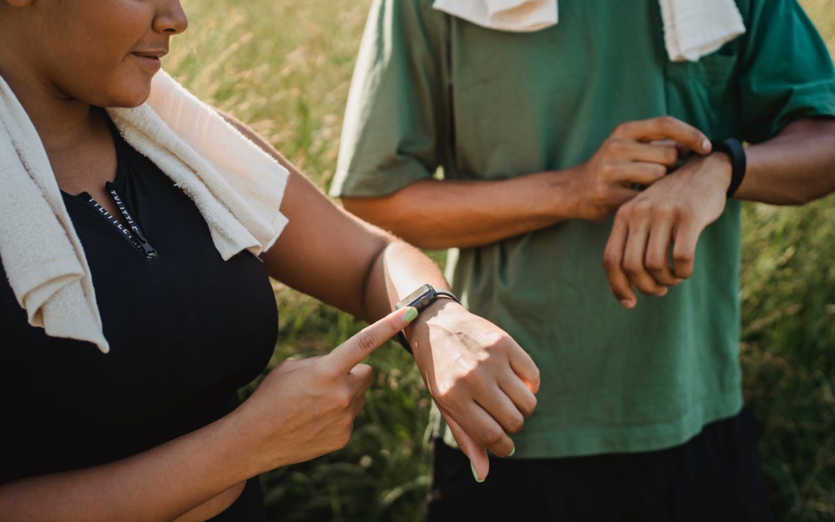 Two people checking their fitness watches while taking a break from a workout outside.