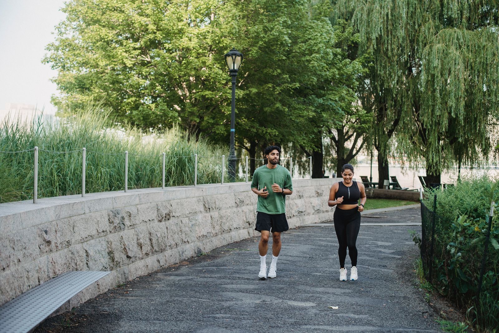 A man and woman jogging together in a lush, green park during the day.