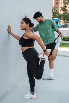 A man and woman stretch against a wall outdoors, promoting fitness and health.