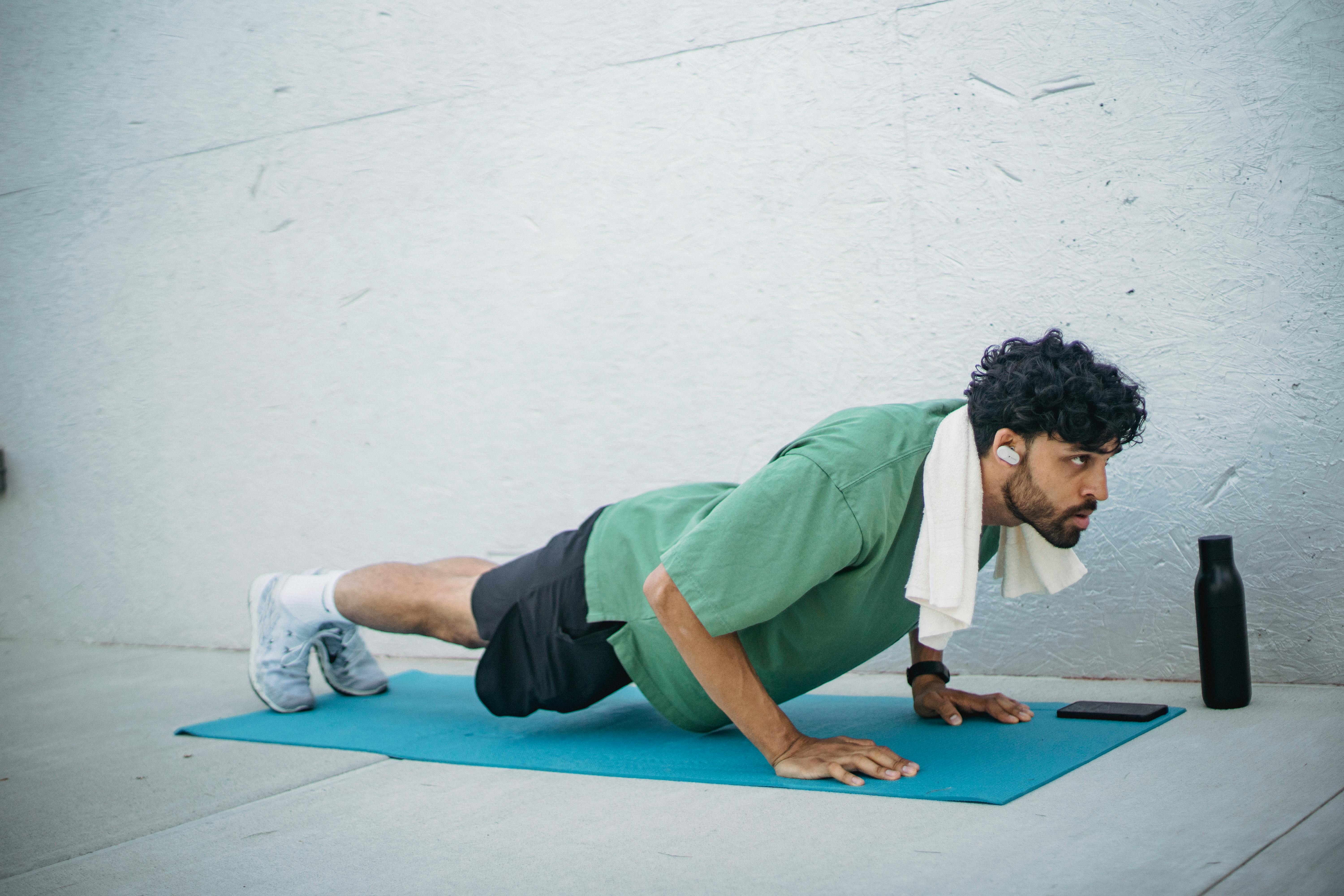 Man doing push-ups on a yoga mat, staying fit with a towel and water bottle nearby.