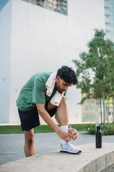 Adult man in sportswear tying shoes outdoors, ready for exercise on a sunny day.