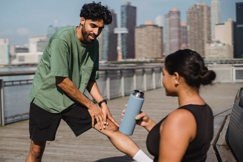 Free Personal trainer assists client on an urban pier with city skyline backdrop. Stock Photo