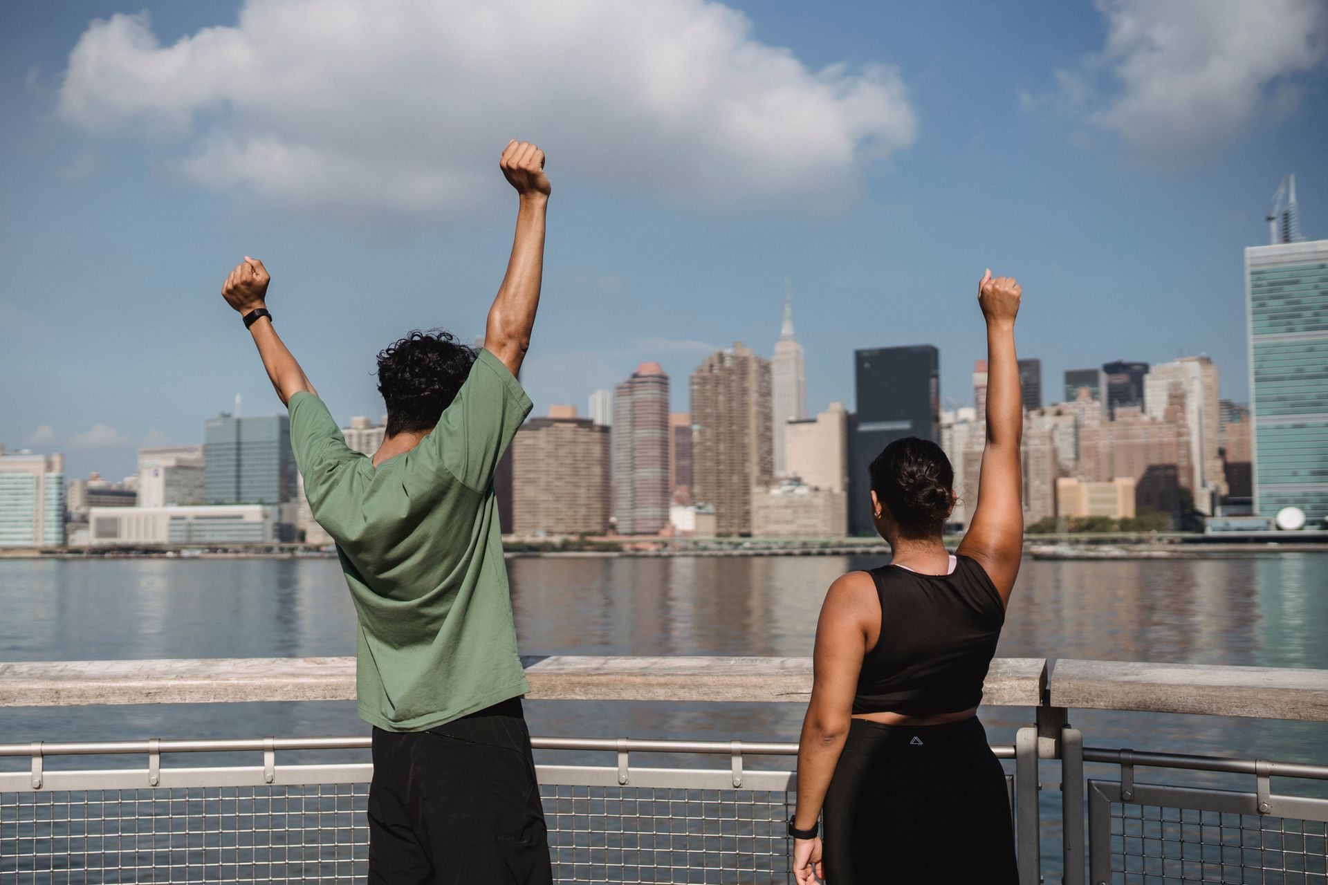 A joyful couple raises their hands in celebration facing a stunning city skyline.