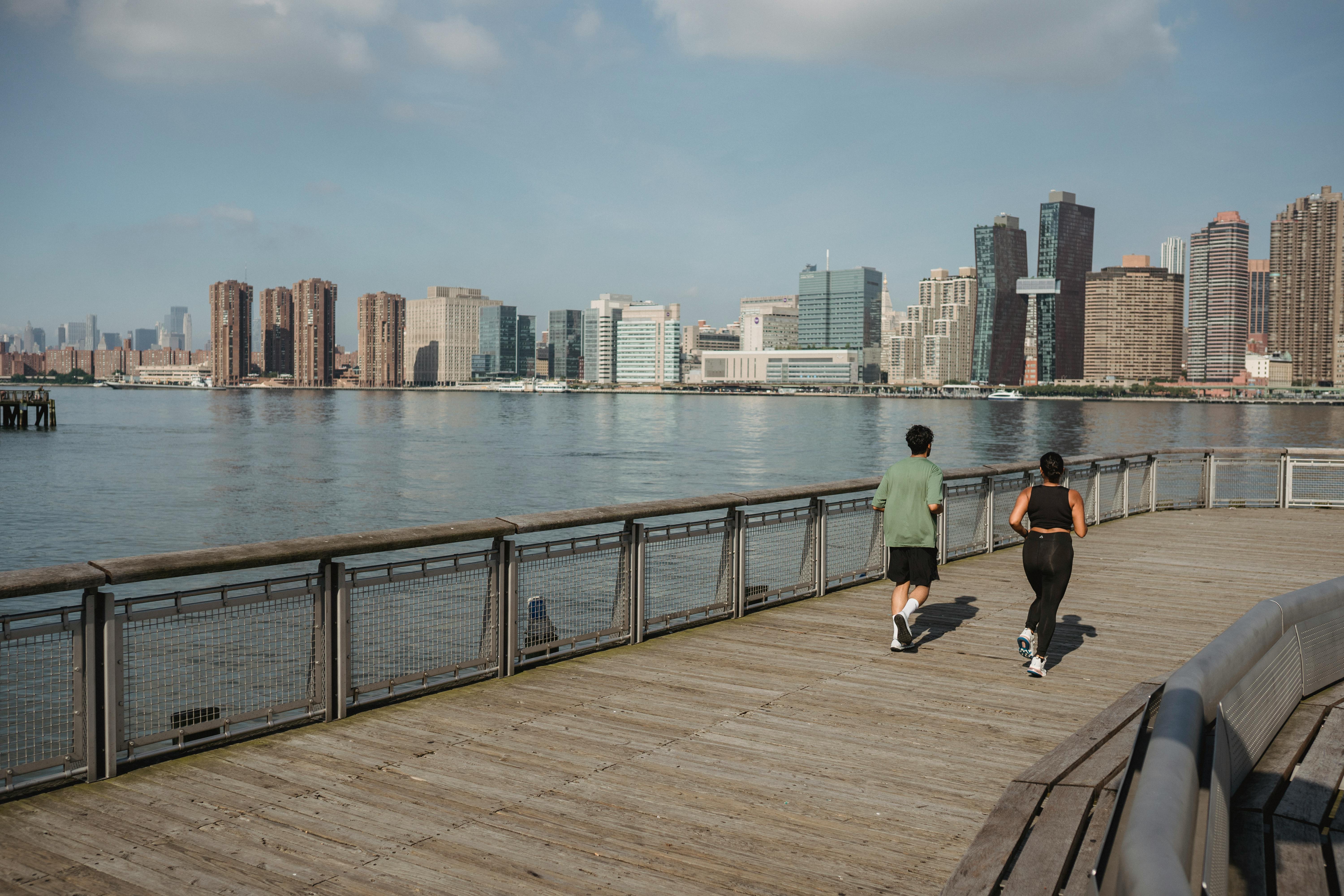 城市天际线背景下，两个人在河畔小路上慢跑