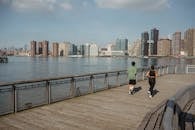 城市天际线背景下，两个人在河畔小路上慢跑