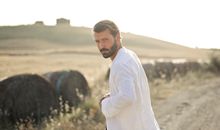 Man in White Robe Standing Beside Black Short Coated Dog