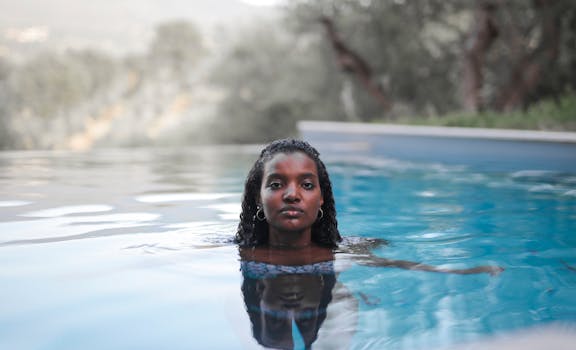A serene portrait of a woman with curly hair relaxing in a calm outdoor swimming pool.