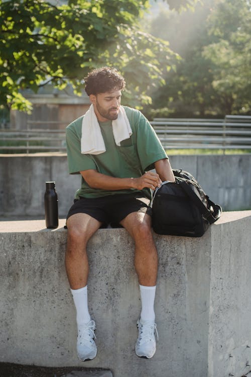 Free A Man in Green Shirt and Black Shorts Sitting on a Concrete Bench Stock Photo