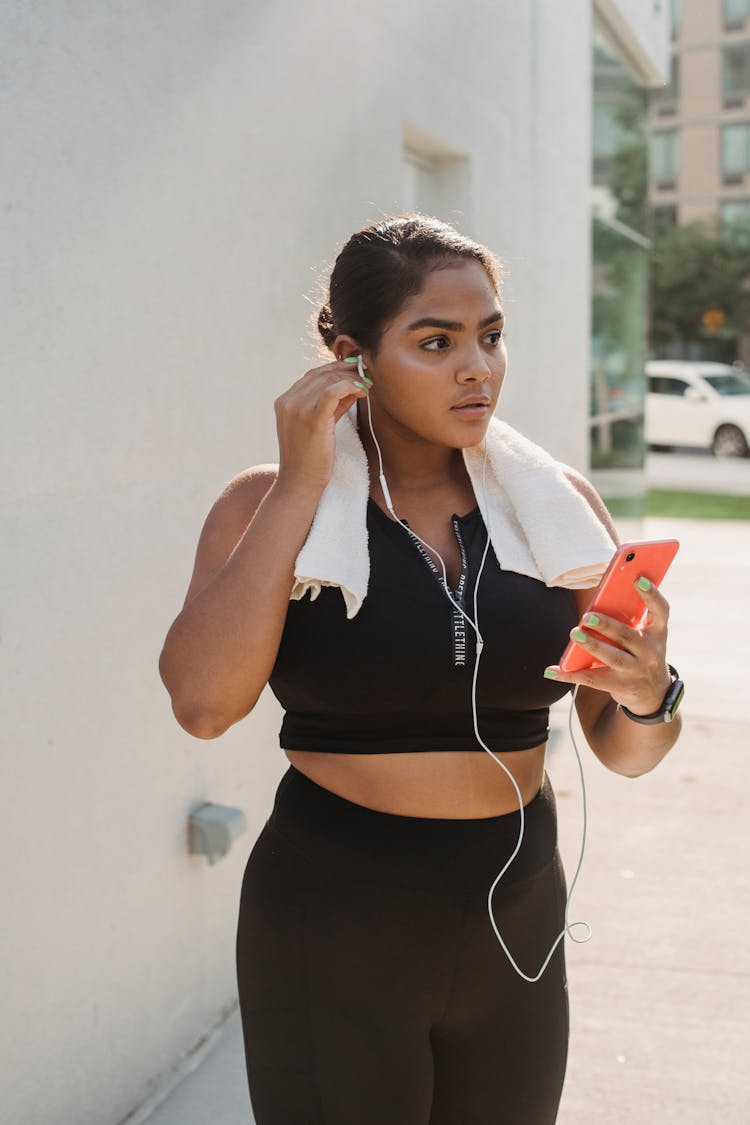 A Woman In Black Clothes Holding Her Mobile Phone While Wearing Earphones On Her Ear