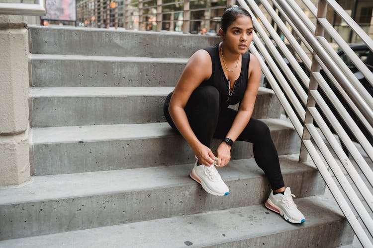 Woman In Sports Clothing Sitting On Stairs And Tying Her Shoe 