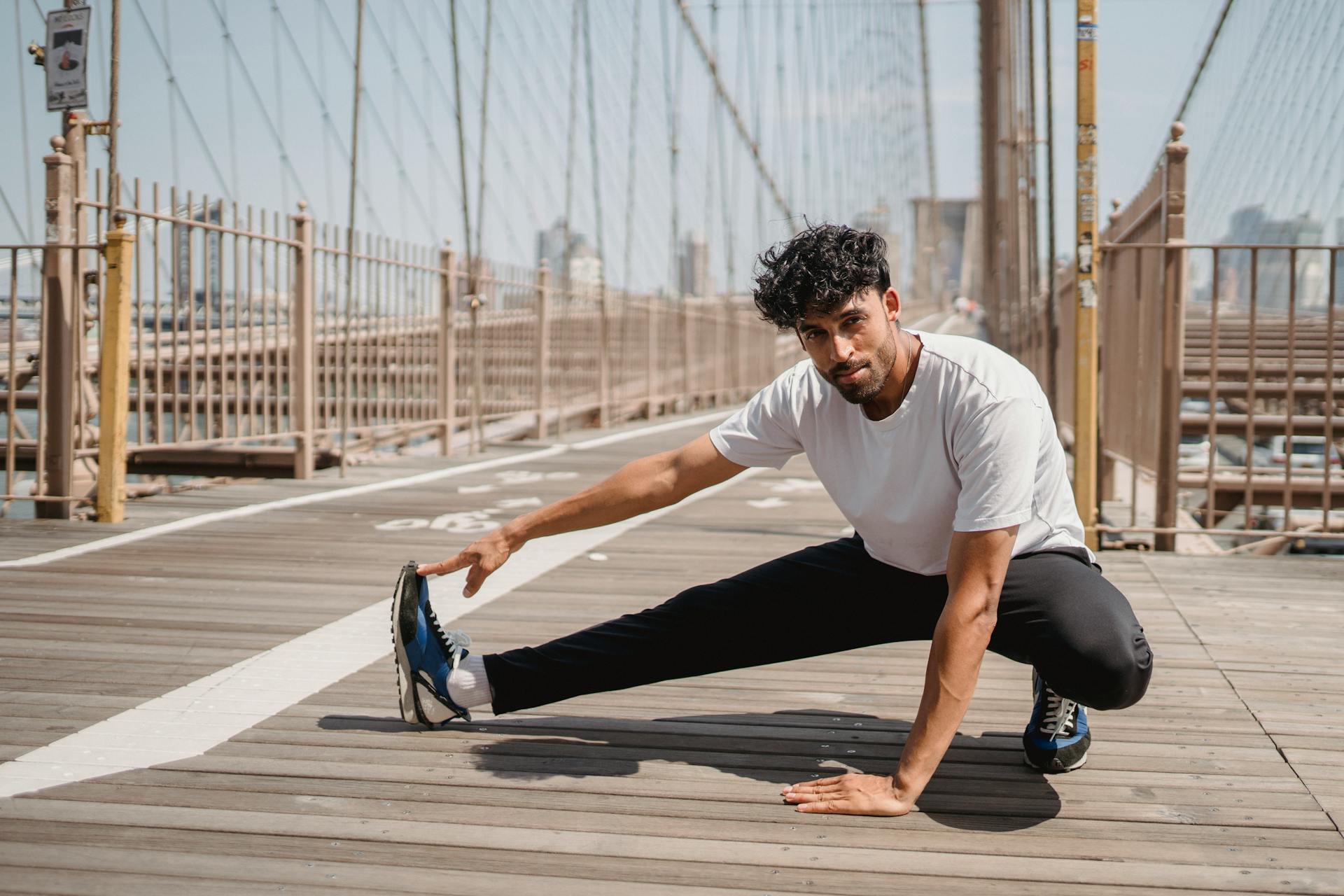 A man in sports attire stretching on Brooklyn Bridge on a sunny day, representing a healthy lifestyle.