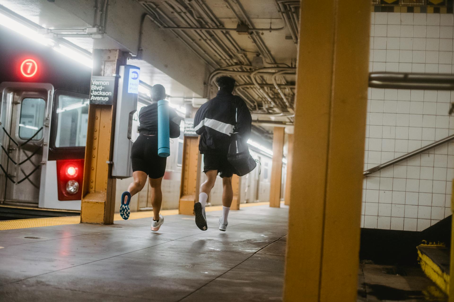 Two athletes running through NYC subway station with yoga mat and sports bag.