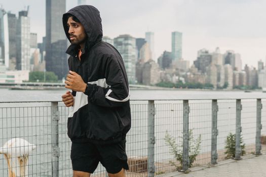 一名男子穿着运动服，沿着河流慢跑，背景是城市天际线