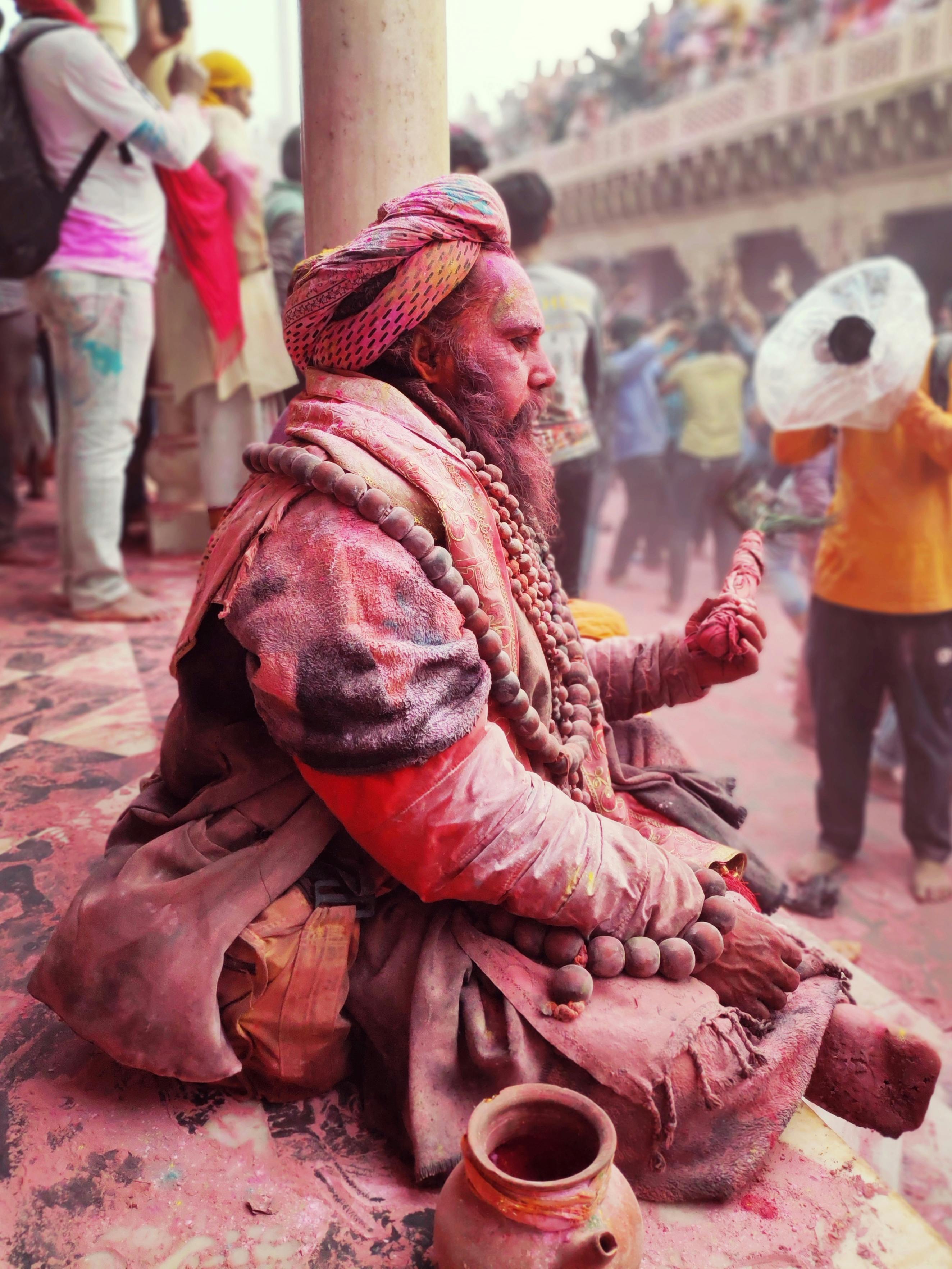 A vibrant Sadhu celebrates Holi, covered in colored powders, in Mathura's lively streets.