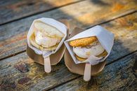 Two ice cream sandwiches served in paper wraps on a rustic wooden table outdoors.