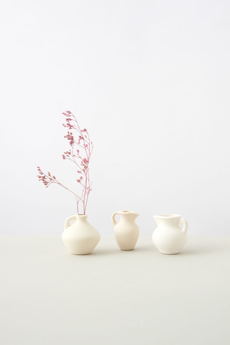 A still life — ceramic vases and dried grasses against a pale ground.