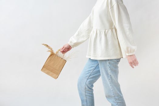 Elegant fashion shot of a woman in denim and beige top carrying dry flowers in a paper bag.