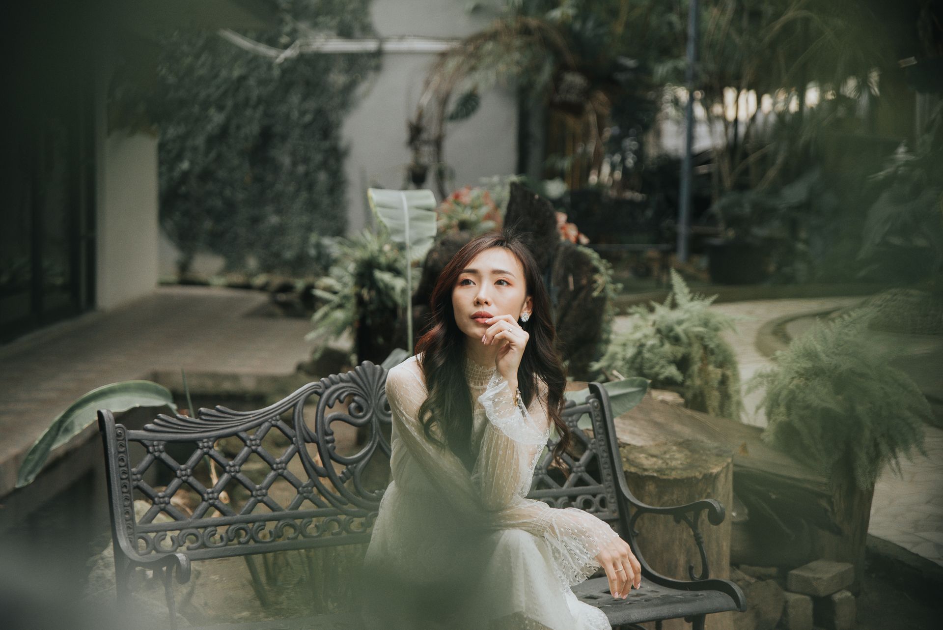 From above of young contemplative ethnic female in stylish outfit touching lips while sitting with crossed legs on bench and looking away