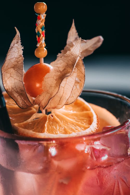 Delicious alcoholic cocktail garnished with ripe orange slice and sour sweet cape gooseberry served in cocktail glass