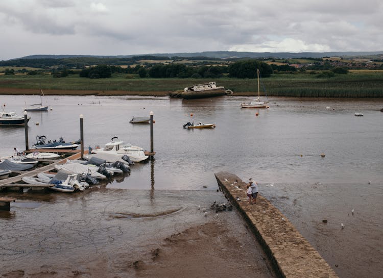 Unrecognizable People On Old Pier Near River With Motor Boats