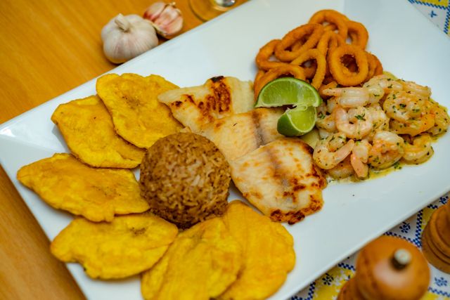 Appetizing seafood platter featuring prawns, fish, tostones, and rice with lime garnish.