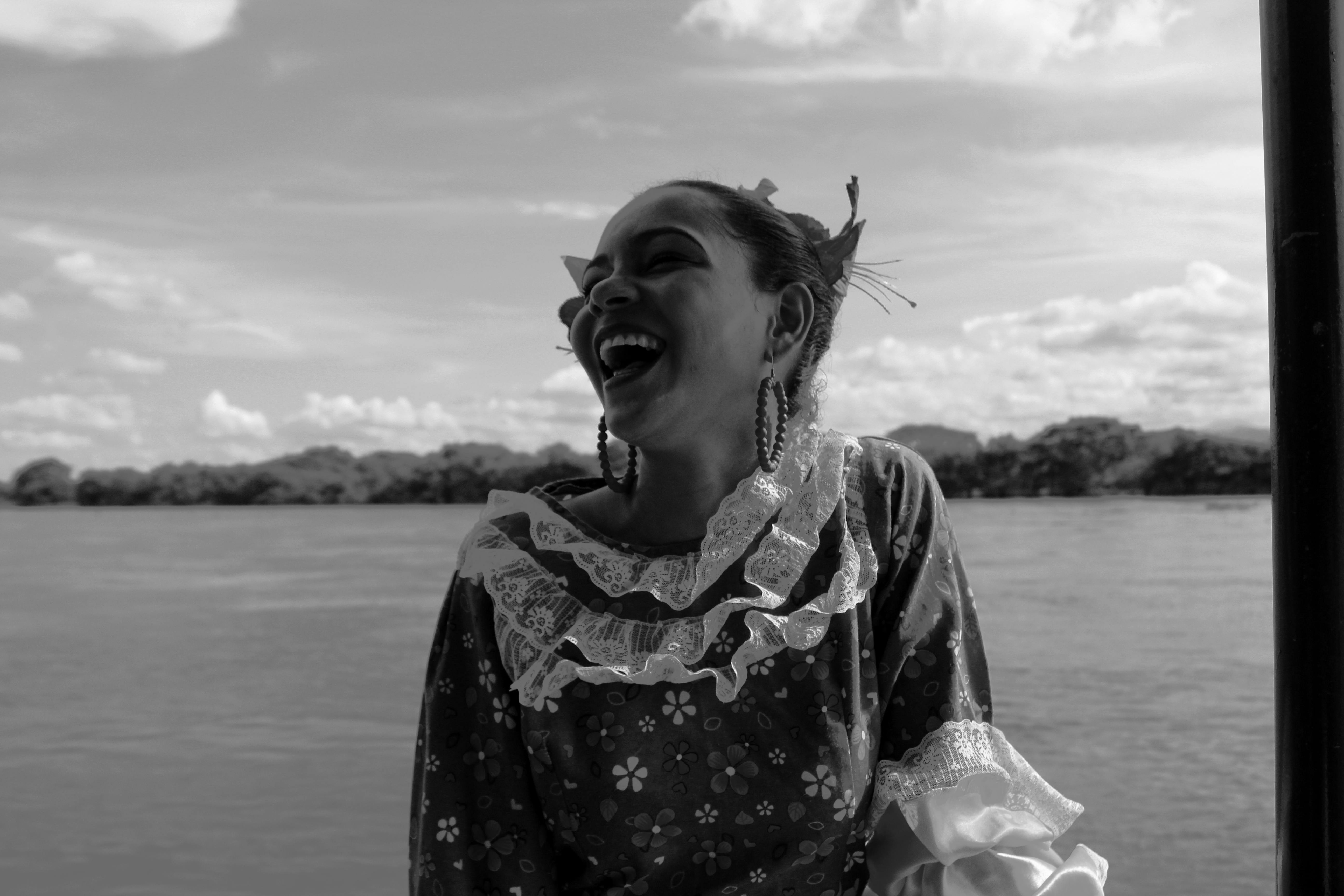 一位身着花卉图案衣服的快乐女人，在河边微笑着，画面十分迷人