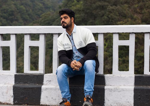 Man in Jacket and Blue Denim Jeans Sitting by the Roadside