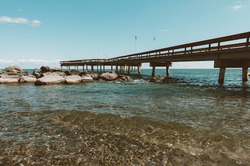 Modern pier on seashore near wet stones and blue clear sky in summer day