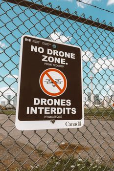 Metal fence with barbed wire in front of city with sign prohibiting to use drones