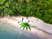 Aerial view to sea and several green canoes and group of people warming-up on sandy beach with green tropical forest before canoeing