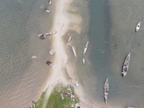 Drone view of traditional wooden boats flowing on rippling sea near sandy beach on sunny day